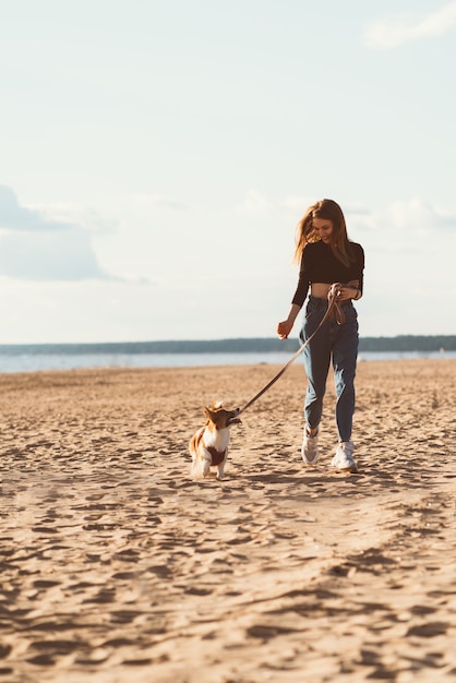 Foto hermosa joven y cachorro corgi corriendo por la playa por el agua.