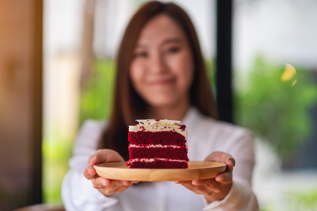 Una hermosa joven camarera asiática o un chef sosteniendo y sirviendo un trozo de pastel de terciopelo rojo en una bandeja de madera