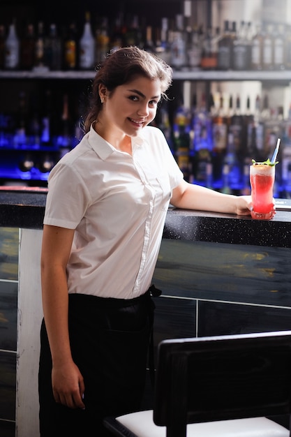 Hermosa joven camarera de pie en un bar con una bebida. Trabajador profesional que brinda el mejor servicio de restaurante.