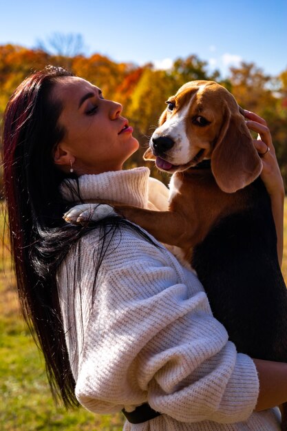 Una hermosa joven camina en el bosque de otoño con dos perros beagle activos