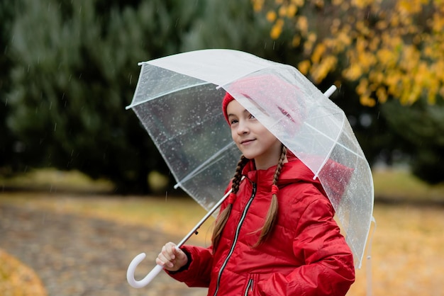 Una hermosa joven camina bajo la lluvia con un paraguas transparente Atmósfera otoñal Clima