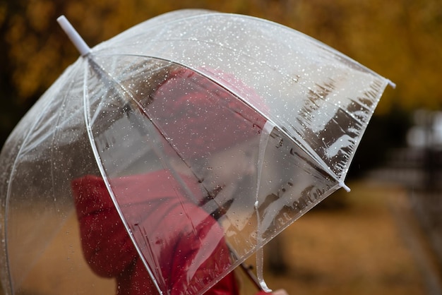 Una hermosa joven camina bajo la lluvia con un paraguas transparente Atmósfera otoñal Clima