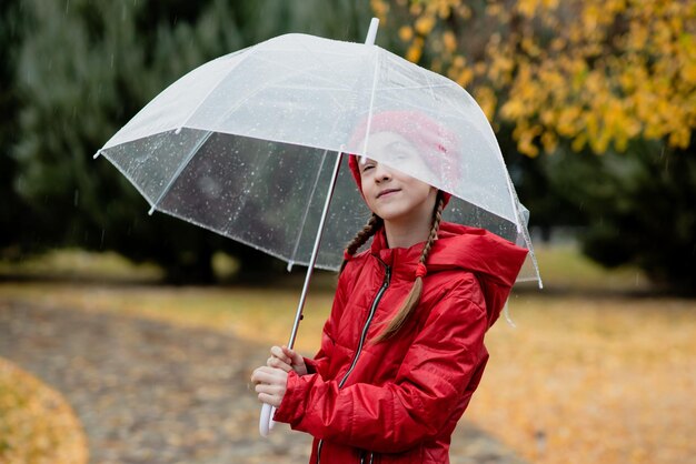 Una hermosa joven camina bajo la lluvia con un paraguas transparente. Otoño. Atmósfera. Clima.