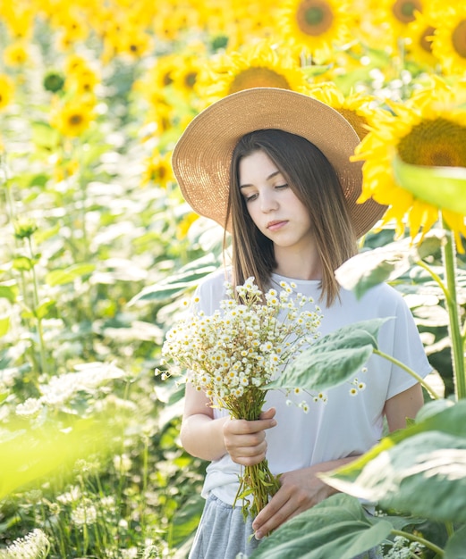 Hermosa joven camina en el verano en un campo con girasoles florecientes