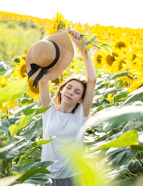 Hermosa joven camina en el verano en un campo con girasoles florecientes