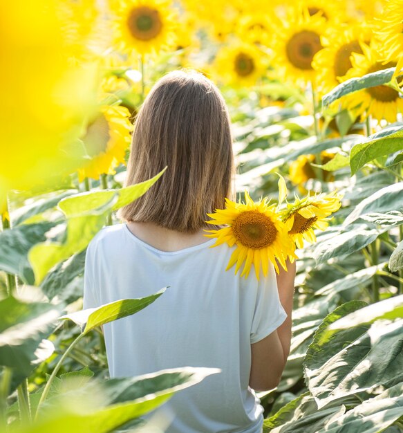 Hermosa joven camina en el verano en un campo con girasoles florecientes