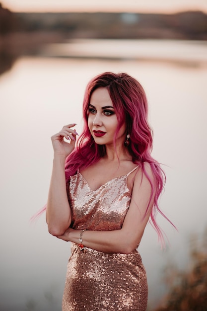 Hermosa joven caminando en los campos de trigo durante la puesta de sol, use un vestido rosa de verano y una corona de flores en la cabeza