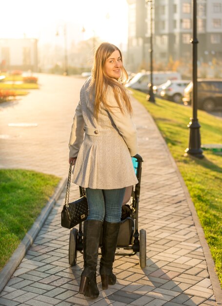 Hermosa joven caminando con cochecito de bebé en el parque