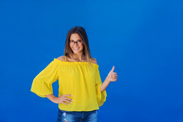 Hermosa joven en camisa amarilla posando delante de la pared azul