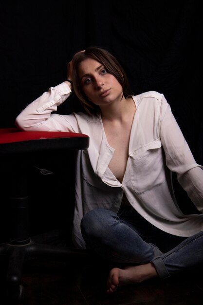 Foto hermosa joven con una camisa blanca y jeans en un fondo negro