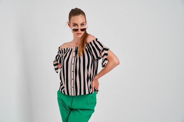 Hermosa joven en camisa a rayas y pantalón verde aislado sobre fondo blanco.