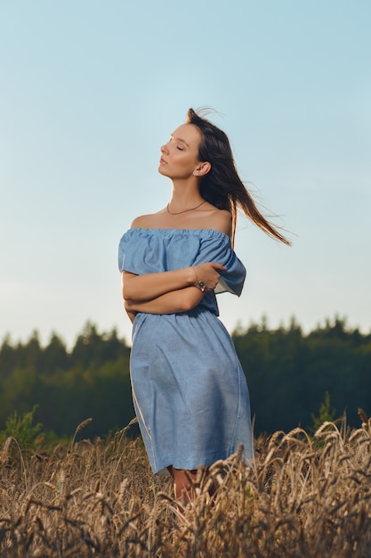 Hermosa joven en campo de trigo al atardecer