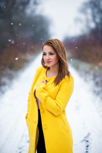 Hermosa joven en una capa amarilla en paisaje nevado