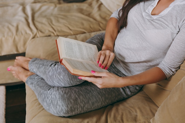 La hermosa joven en casa sentada en el sofá, relajándose en su sala de estar y leyendo un libro