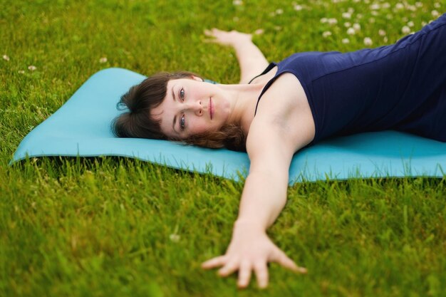 Hermosa joven caucaisana trabajando al aire libre en la vista superior de la estera azul Jathara Parivartanasana