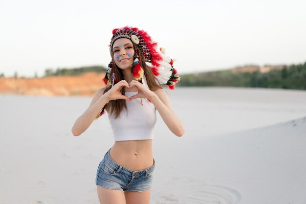 Una hermosa joven caucásica con una blusa blanca en la cabeza lleva un sombrero indio. Roach está en el desierto. Felices vacaciones de humor.