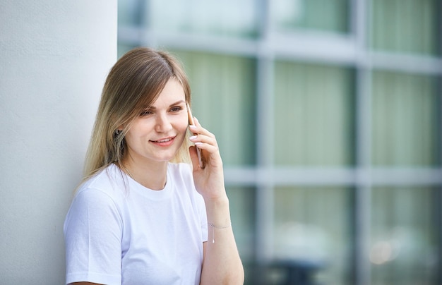 Hermosa joven caucásica está hablando por teléfono en la calle en la ciudad en un día de verano Primer plano