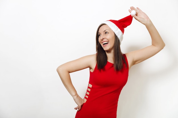 La hermosa joven caucásica feliz con piel sana y sonrisa encantadora con vestido rojo con sombrero de Navidad sobre fondo blanco. Retrato aislado de la muchacha de Santa. Concepto de vacaciones de año nuevo 2018