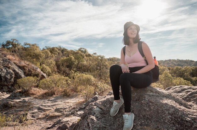 Hermosa joven caucásica latina cansada caminando por la montaña descansando sentada en una piedra