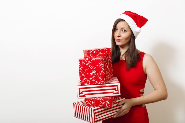 Hermosa joven caucásica molesta frustrada y triste mujer vestida con vestido rojo y sombrero de Navidad con cajas de regalo sobre fondo blanco. Niña de Santa con presente aislado. Concepto de vacaciones de año nuevo 2018.