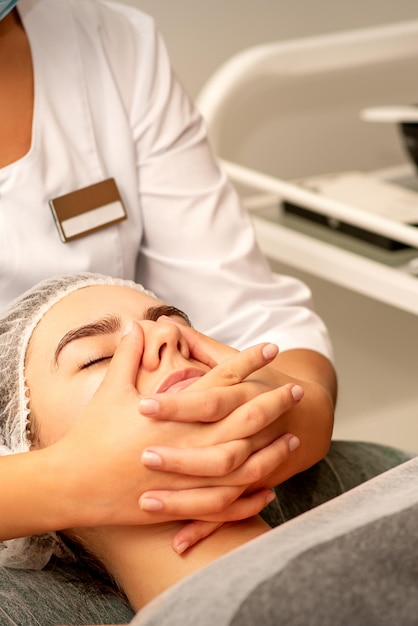 Hermosa joven caucásica con los ojos cerrados recibiendo un masaje facial en un salón de belleza