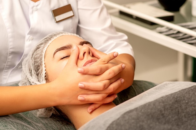 Hermosa joven caucásica con los ojos cerrados recibiendo un masaje facial en un salón de belleza