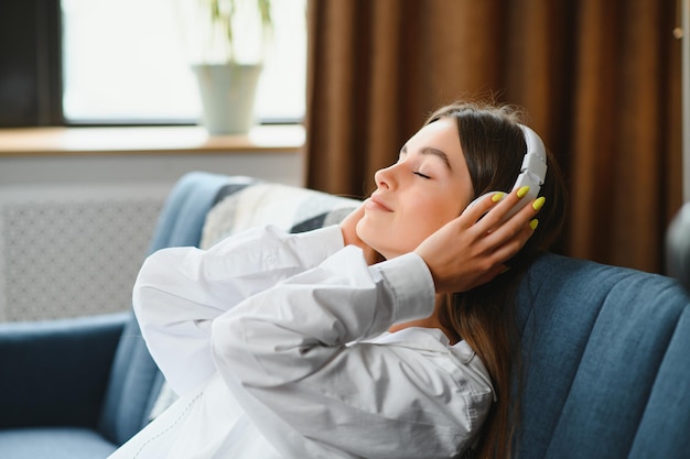 Hermosa joven caucásica con ropa informal disfrutando de la música y sonriendo mientras descansa en casa Mujer joven con auriculares usando una computadora portátil en casa