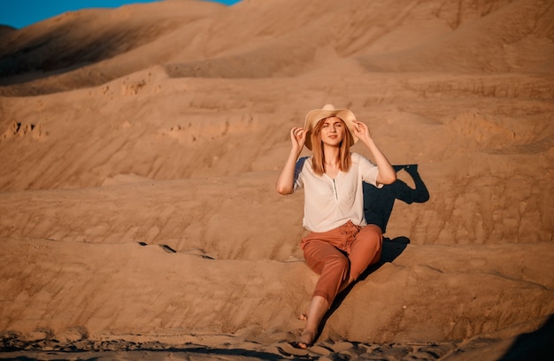 Foto hermosa joven caucásica sola está en un calor. puesta de sol en el desierto. chica caminando sobre arena dorada.