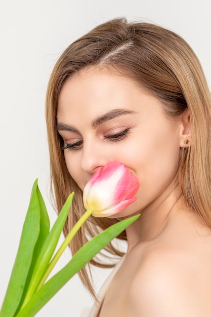 Hermosa joven caucásica con un tulipán en busca de una flor sobre un fondo blanco.