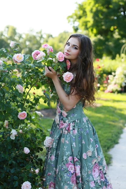 Hermosa joven cerca de un arbusto con rosas en el parque