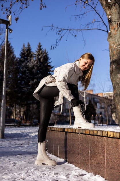 Una hermosa joven con una chaqueta blanca y botas de cuero blancas camina en un parque nevado