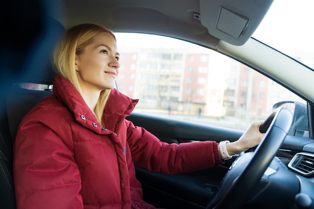 Una hermosa joven con una chaqueta roja conduce un auto