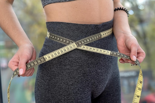 Foto hermosa joven con cintura delgada y estómago plano mide la circunferencia de la cintura con una cinta métrica el concepto de centímetros del cuerpo concepto de dieta y deporte