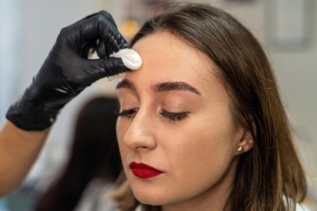 Hermosa joven cliente se está limpiando las cejas después de pintarlas