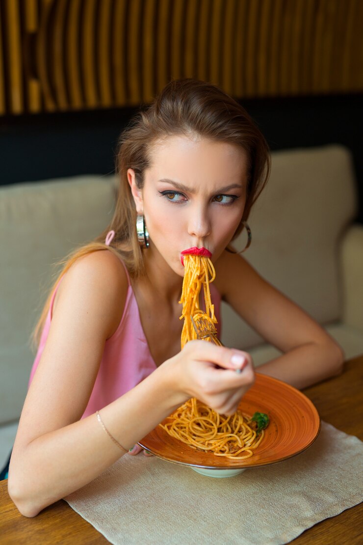 Hermosa joven come espaguetis en un restaurante
