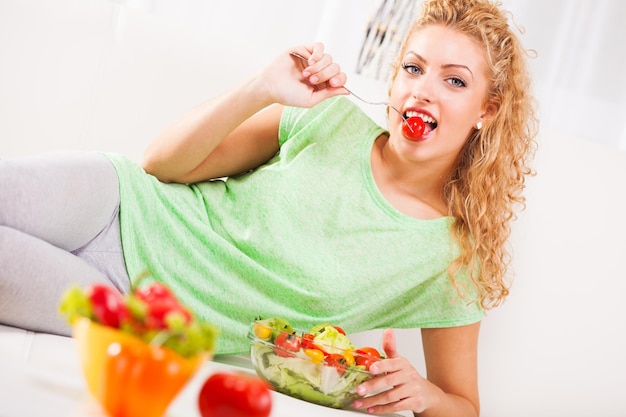 Hermosa joven comiendo tomate pequeño con tenedor