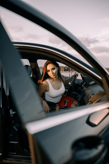 Foto hermosa joven conduciendo un coche por la noche bajo el sol del atardecer en un estacionamiento vacío