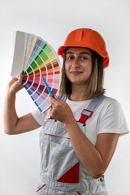 Hermosa joven constructora se encuentra en un casco y con muestras de color en las manos para elegir el color de la pared La profesión de una mujer constructora aislada en el fondo blanco