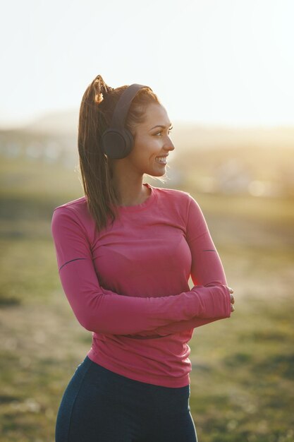 Foto hermosa joven corredora escuchando música y preparándose para trotar al atardecer en las montañas.