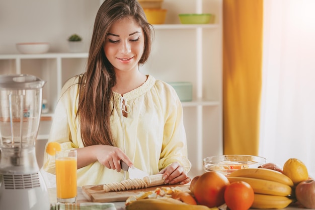 Hermosa joven cortando plátano en la cocina.