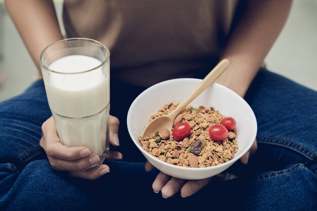 Hermosa joven cuida su salud comiendo leche con granola de granos múltiples en la mañana