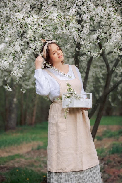 Una hermosa joven en el delantal disfruta de la vida en un jardín floreciente de primavera con árboles florecientes