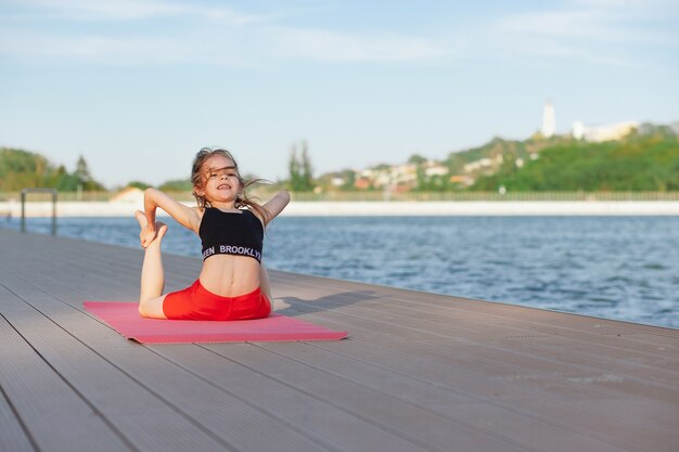 Hermosa joven delgada haciendo yoga o ejercicio gimnástico junto al lago Estilo de vida saludable