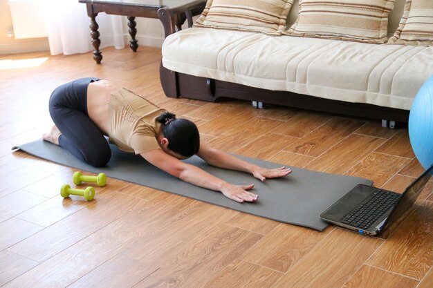 Una hermosa joven deportista en leggings y un top va a hacer deporte en casa