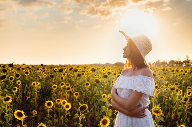 Hermosa joven disfrutando de la naturaleza en el campo de girasoles al atardecer