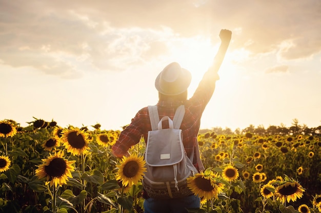 Hermosa joven disfrutando de la naturaleza en el campo de girasoles al atardecer