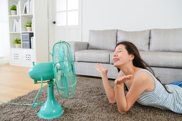 Foto hermosa joven disfrutando del viento fresco del ventilador eléctrico en la sala de estar.