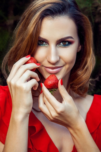 Hermosa joven divertida feliz con vestido rojo y maquillaje con fresa en verano en el