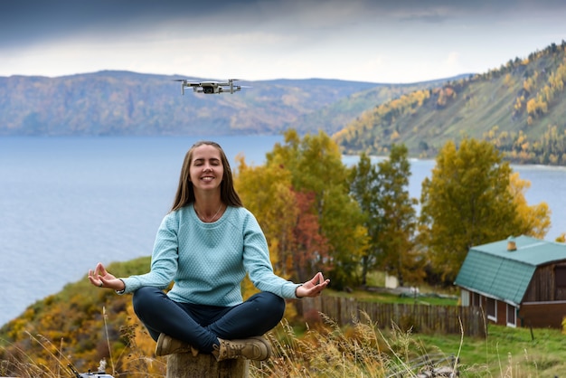 Hermosa joven divirtiéndose con un mini drone al aire libre en pose de loto