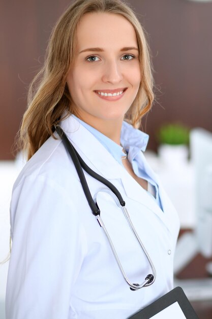 Hermosa joven doctora sonriente parada en un hospital con su colega en el fondo.